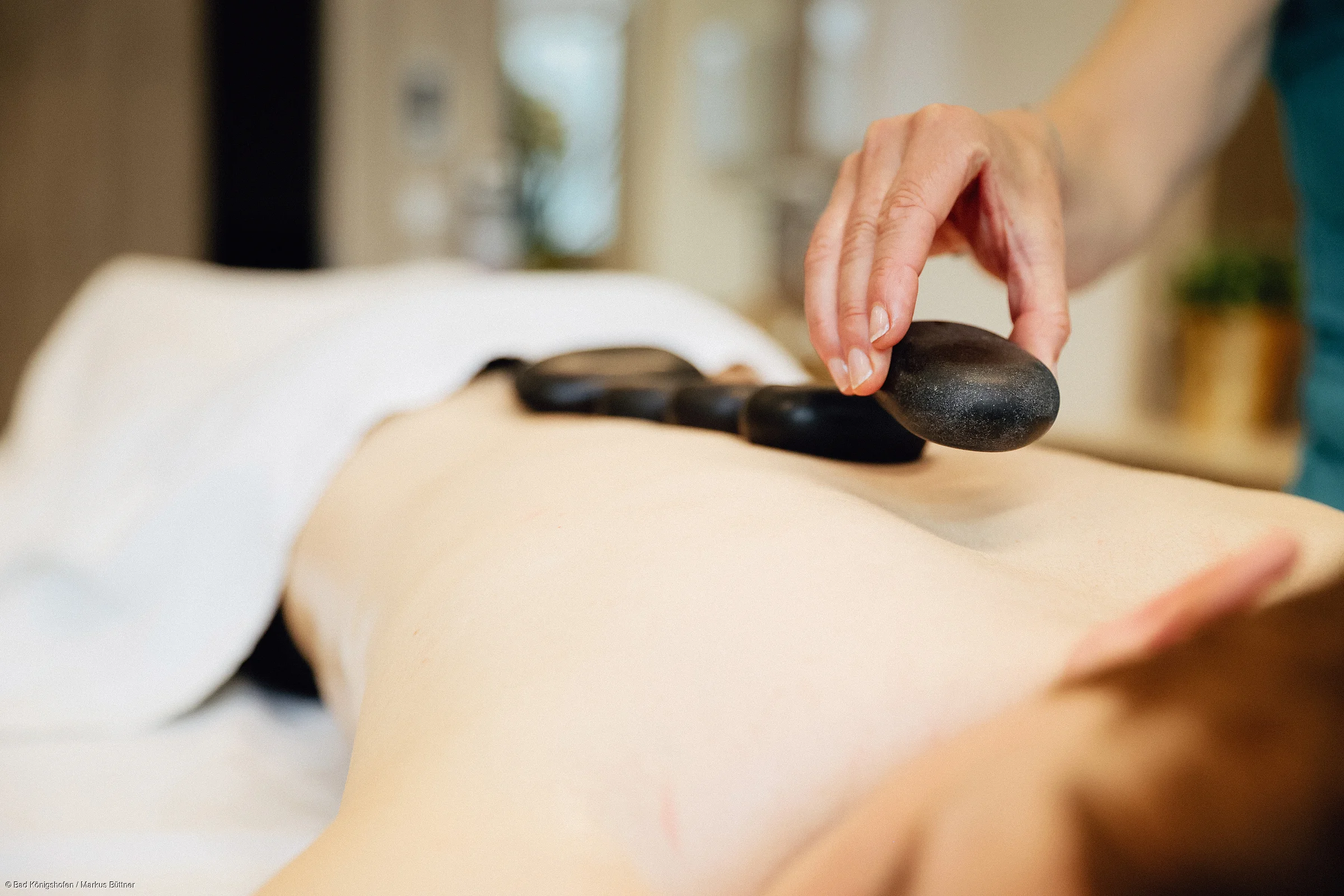 Hand legt schwarzen Hot-Stone auf nackten Rücken einer liegenden Person bei Massage.