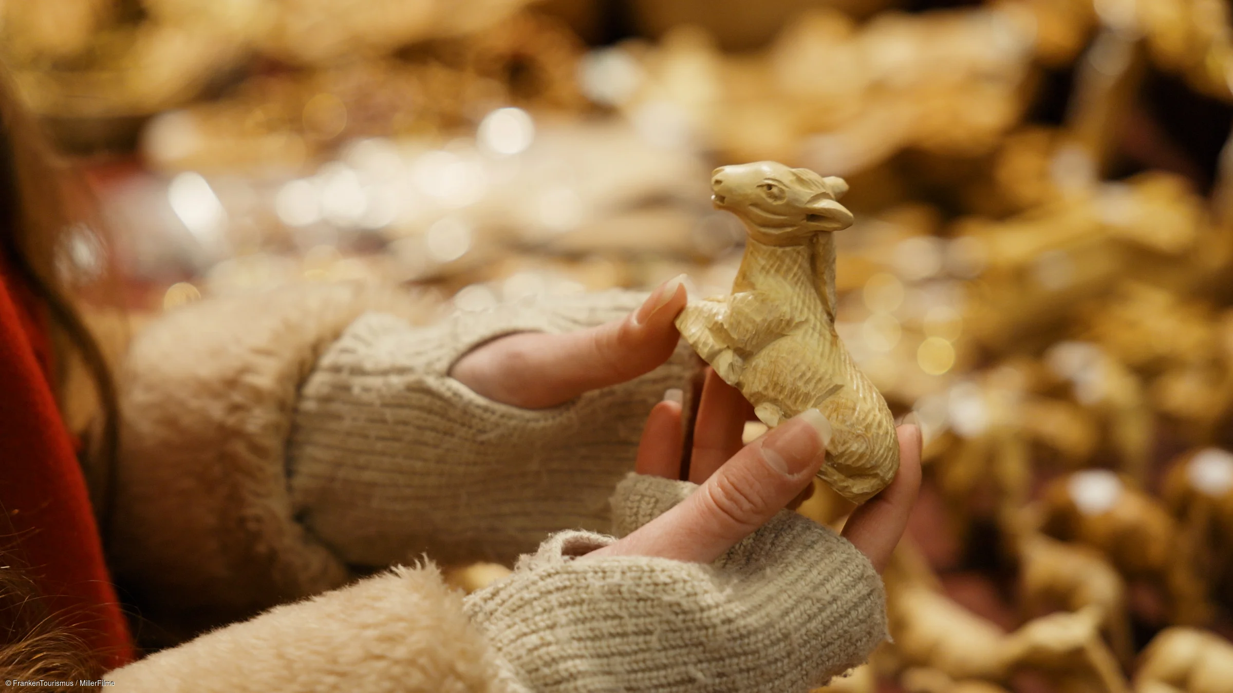 Hände mit grauen Handschuhen halten eine kleine geschnitzte Holzfigur eines Esels, unscharfer Hintergrund.