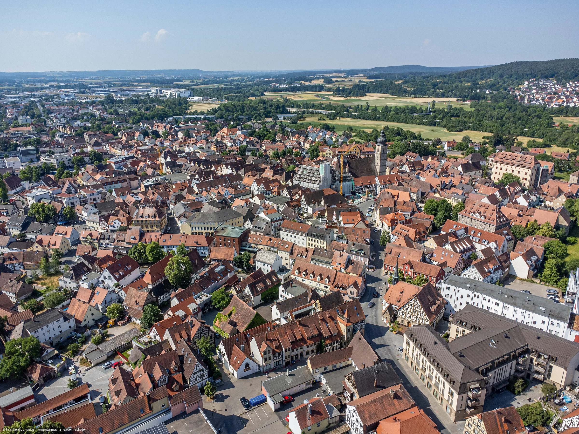 Luftaufnahme einer Stadt mit dicht bebauten Häusern und Feldern im Hintergrund an einem klaren Tag.