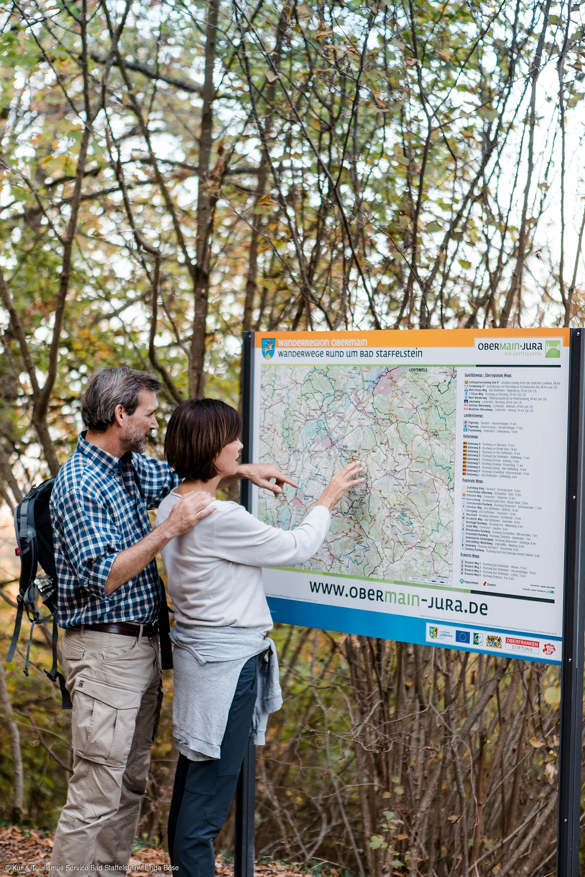 Zwei Wanderer lesen eine Wanderkarte an einem Infostand im Wald im Herbst.