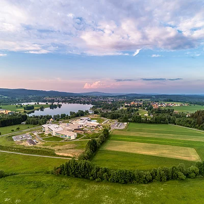 Luftaufnahme von Feldern, einem See und einem Gebäudekomplex unter bewölktem Himmel bei Abendlicht