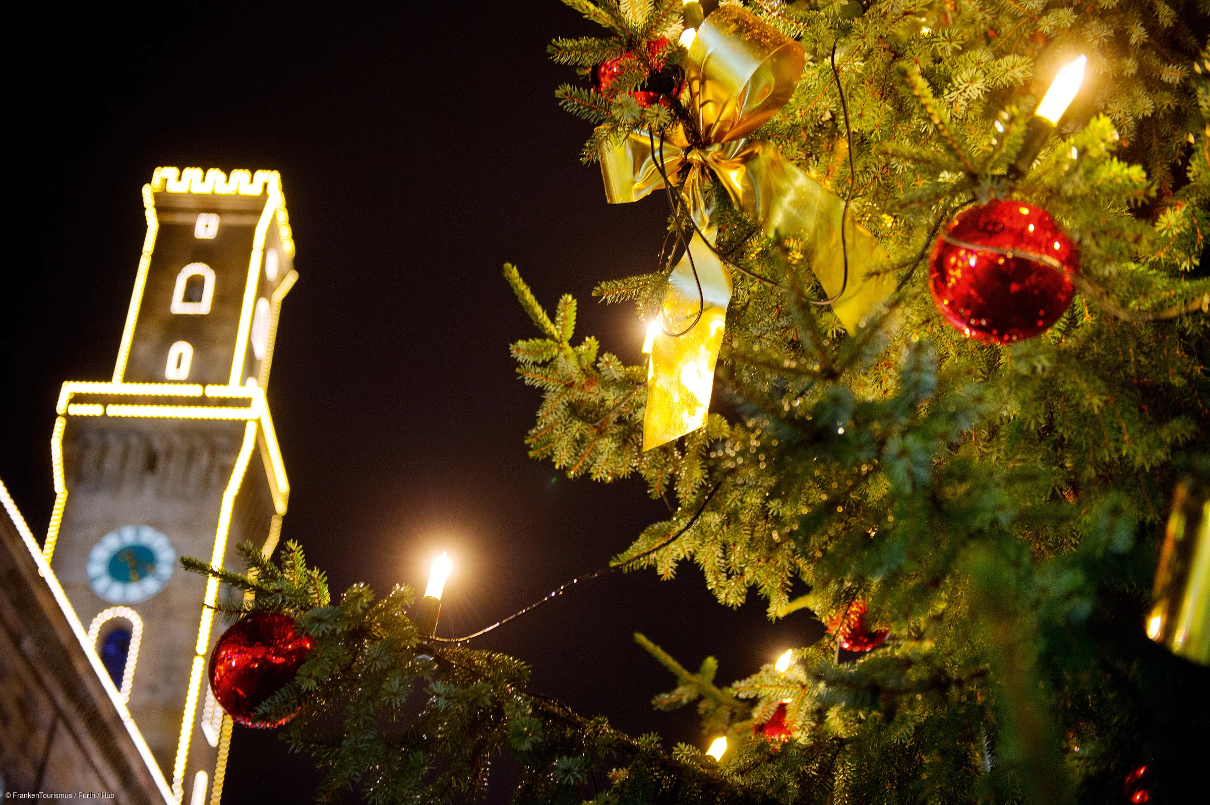 Weihnachtsbaum mit roten Kugeln und Lichtern, beleuchteter Rathausturm im Hintergrund bei Nacht