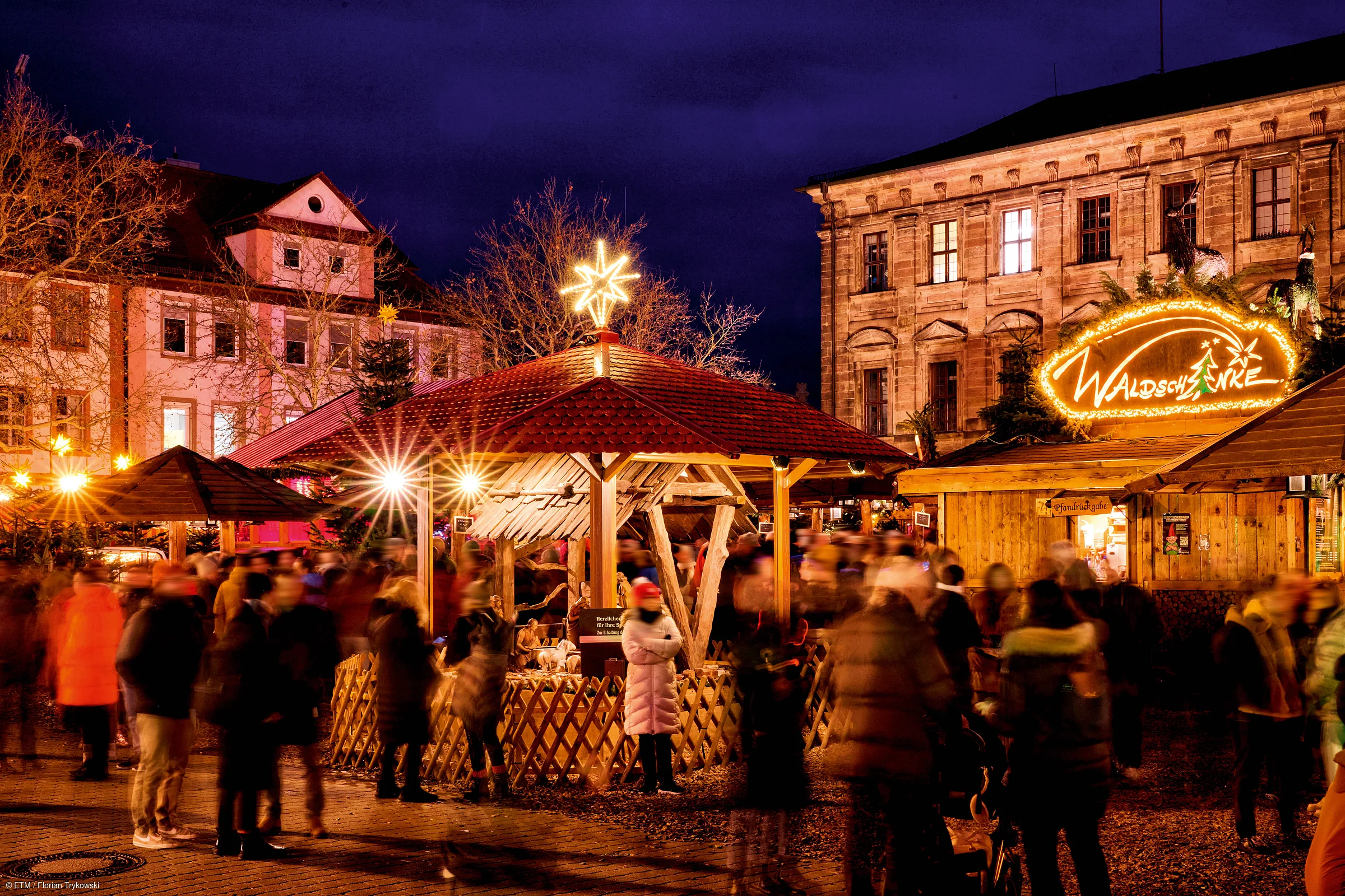 Weihnachtsmarkt bei Nacht mit beleuchteten Ständen und Menschen in Winterkleidung vor historischen Gebäuden