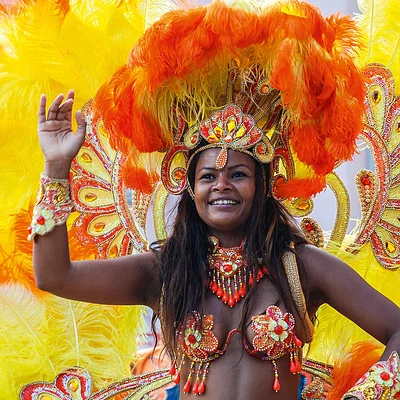 Frau in farbenfrohem Karnevalskostüm mit orangen und gelben Federn und Schmuck tanzt und lächelt.
