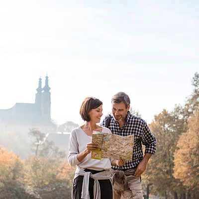 Paar steht im Park und betrachtet gemeinsam eine Wanderkarte an einem herbstlichen Tag.