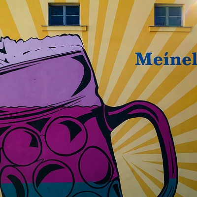 Wandgemälde mit großem lila Bierkrug und Schriftzug „Meinel Bräu“ auf gelb gestreiftem Hintergrund