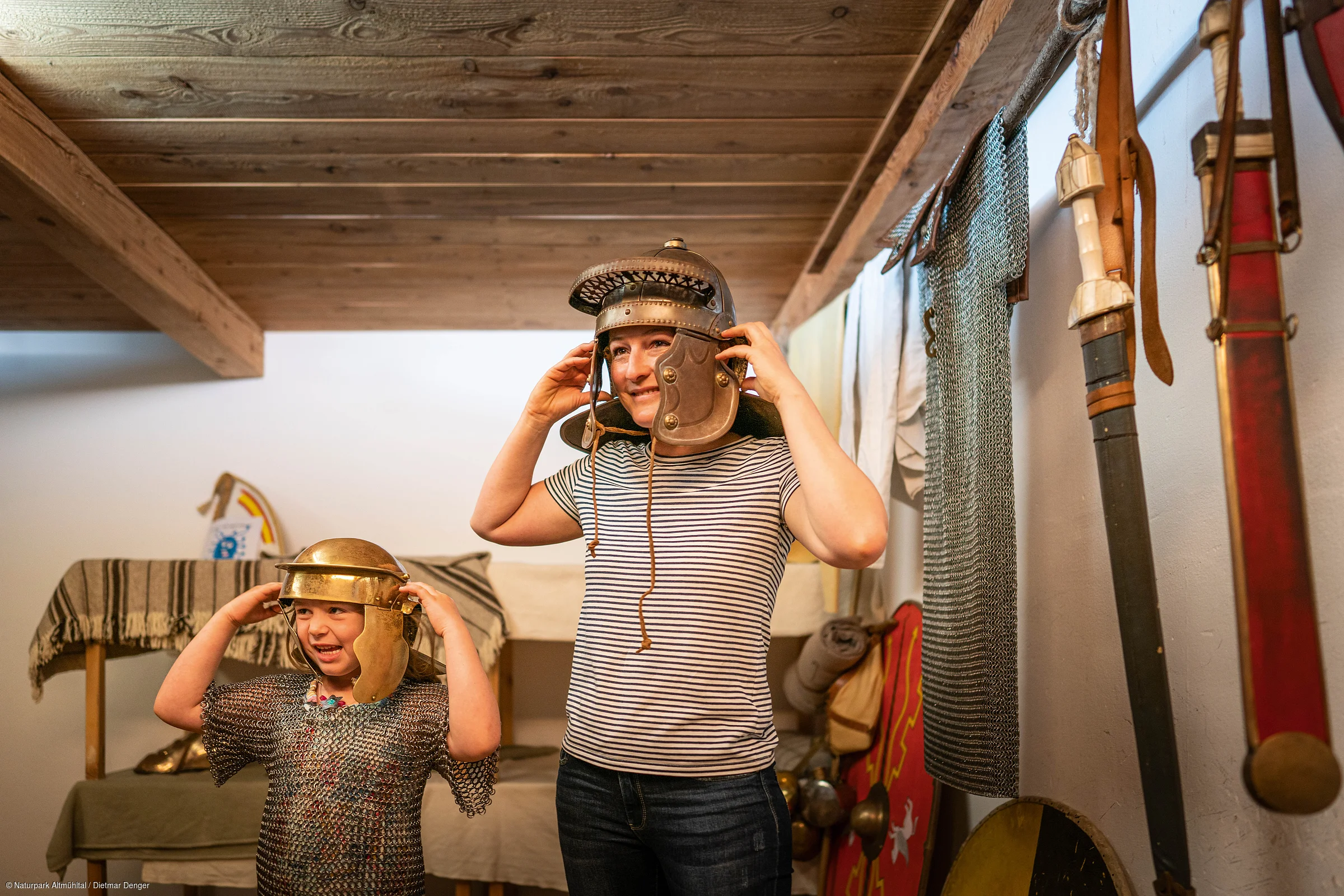 Kinder probieren antike Helme und Kettenhemden in einem Raum mit historischen Waffen an.