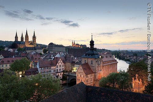Blick auf historische Altstadt mit Fachwerkhäusern, Fluss und Kirchen bei Abenddämmerung.