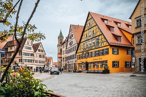 Altstadtstraße mit Fachwerkhäusern, Kopfsteinpflaster, Autos und Fußgängern bei bewölktem Himmel