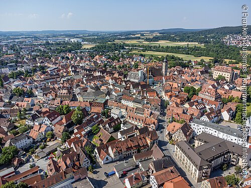 Luftaufnahme einer Stadt mit dicht bebauten Häusern und Feldern im Hintergrund an einem klaren Tag.