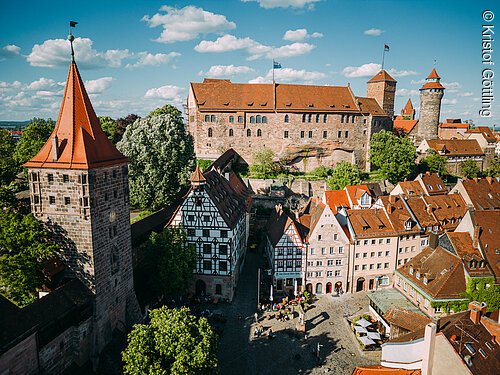 Blick auf mittelalterliche Gebäude und Burg mit roten Dächern in einer Stadt bei Sonnenschein und blauem Himmel