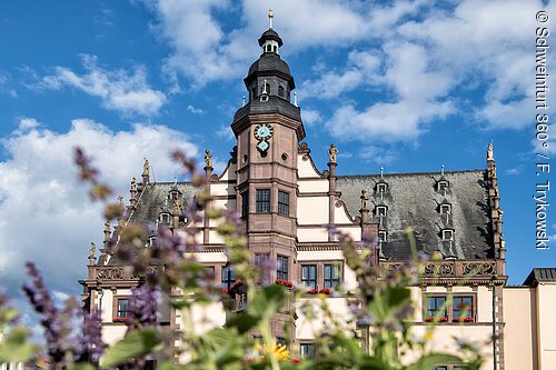 Prächtiges Rathaus mit dunkel gedecktem Dach und Turm, davor Blumen