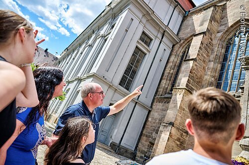 Stadtführung (Ansbach, Romantisches Franken) Gruppe von Menschen betrachtet und zeigt auf ein historisches Gebäude mit großen Fenstern und Steinmauern.
