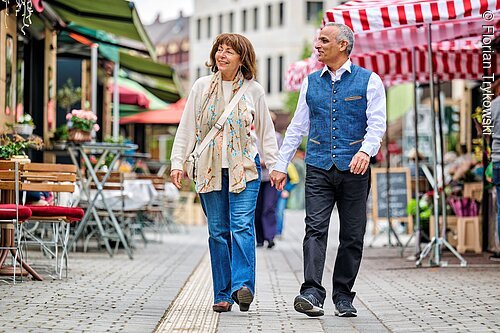 Grüner Markt (Fürth, Städteregion Nürnberg) Älteres Paar hält Händchen und spaziert auf gepflastertem Marktweg mit Ständen und Sitzgelegenheiten.