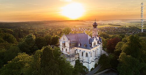 Luftaufnahme eines Schlosses mit Turm umgeben von Bäumen bei Sonnenuntergang in ländlicher Umgebung.