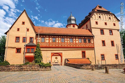 Historisches Gebäude mit Fachwerk und rotem Dach bei blauem Himmel, Pflastersteinweg im Vordergrund.
