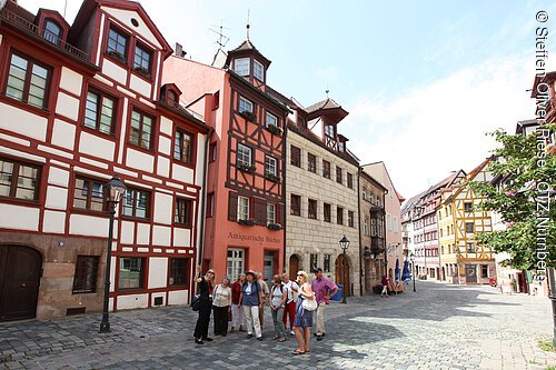 Gruppe von Menschen vor Fachwerkhäusern in einer gepflasterten Straße bei Tageslicht.