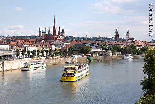 Fluss mit Ausflugsschiffen vor Stadt mit historischen Gebäuden und Kirchtürmen bei Tageslicht