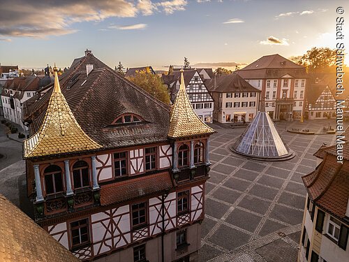Altstadt mit Fachwerkhäusern und golden glänzenden Türmchen, moderner Glaspyramide und gepflastertem Platz bei Sonnenuntergang