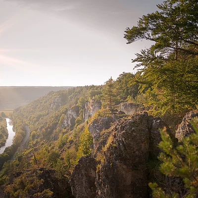 Sonnenaufgang über bewaldeten Felsen mit Fluss und Tal im Hintergrund, Blick von oben