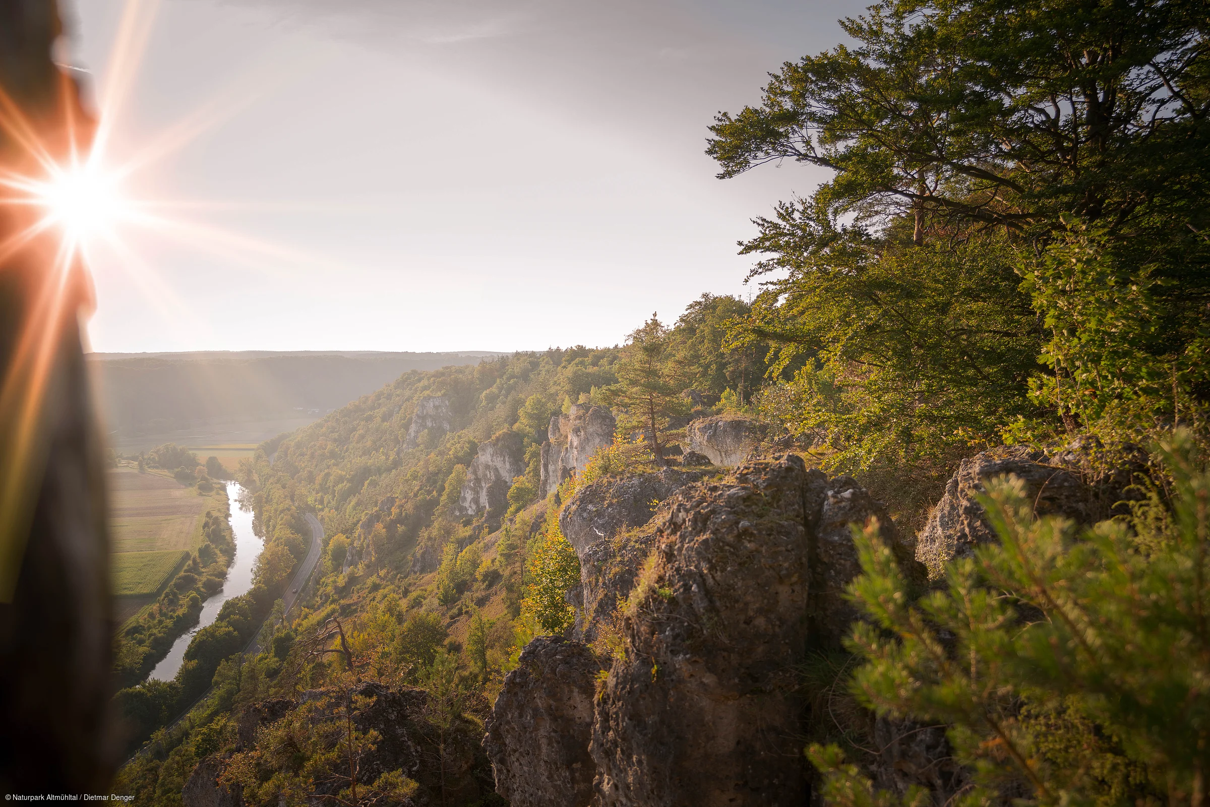 Sonnenaufgang über bewaldeten Felsen mit Fluss und Tal im Hintergrund, Blick von oben