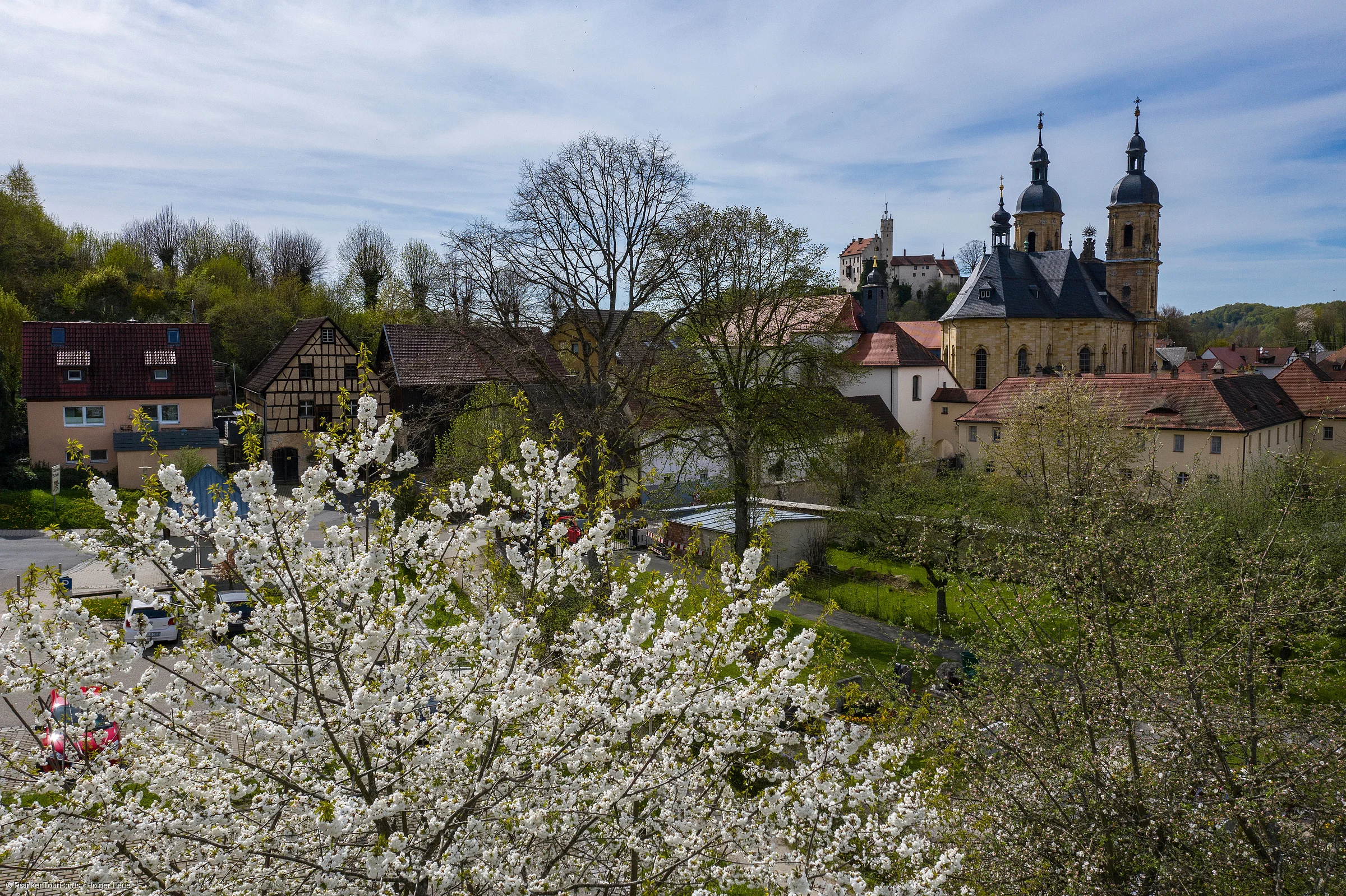 Blick auf ein Dorf mit blühenden Bäumen, Fachwerkhäusern und einer Kirche mit zwei Türmen.