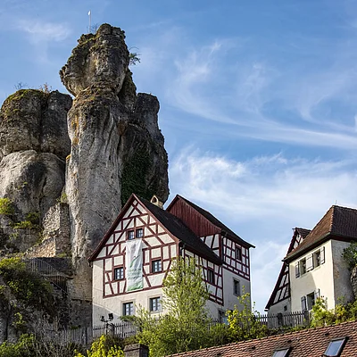 Fachwerkhäuser neben großen Felsen unter blauem Himmel mit dünnen Wolken.