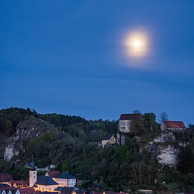 Dorf bei Nacht mit beleuchteten Häusern, Hügeln und Vollmond am klaren Himmel