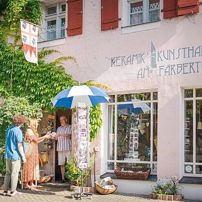 Drei Personen vor einem Laden mit Schriftzug „Keramik Kunsthandwerk am Färberturm“ und grüner Pflanzenwand