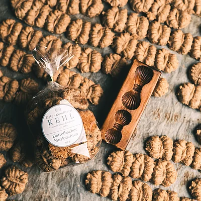 Verpackte und lose Dettelbacher Muskatzinen-Kekse neben einem Holzmodel mit Muskatzinen-Motiv auf Backpapier.