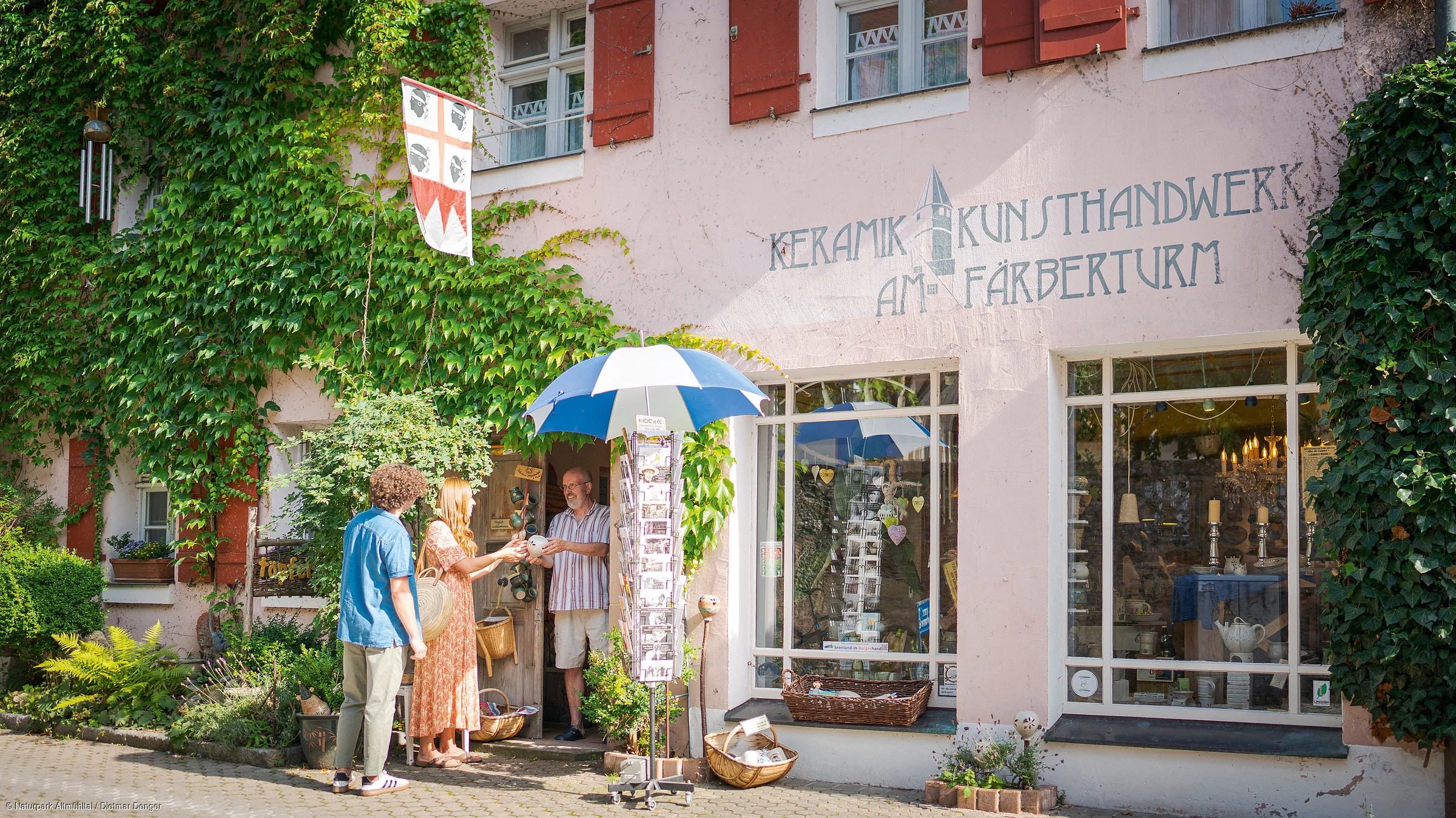 Drei Personen vor einem Laden mit Schriftzug „Keramik Kunsthandwerk am Färberturm“ und grüner Pflanzenwand