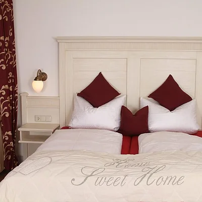 Zweibettzimmer mit weißen Bettdecken, roten Kissen, Nachttischen und roten Vorhängen mit Muster.