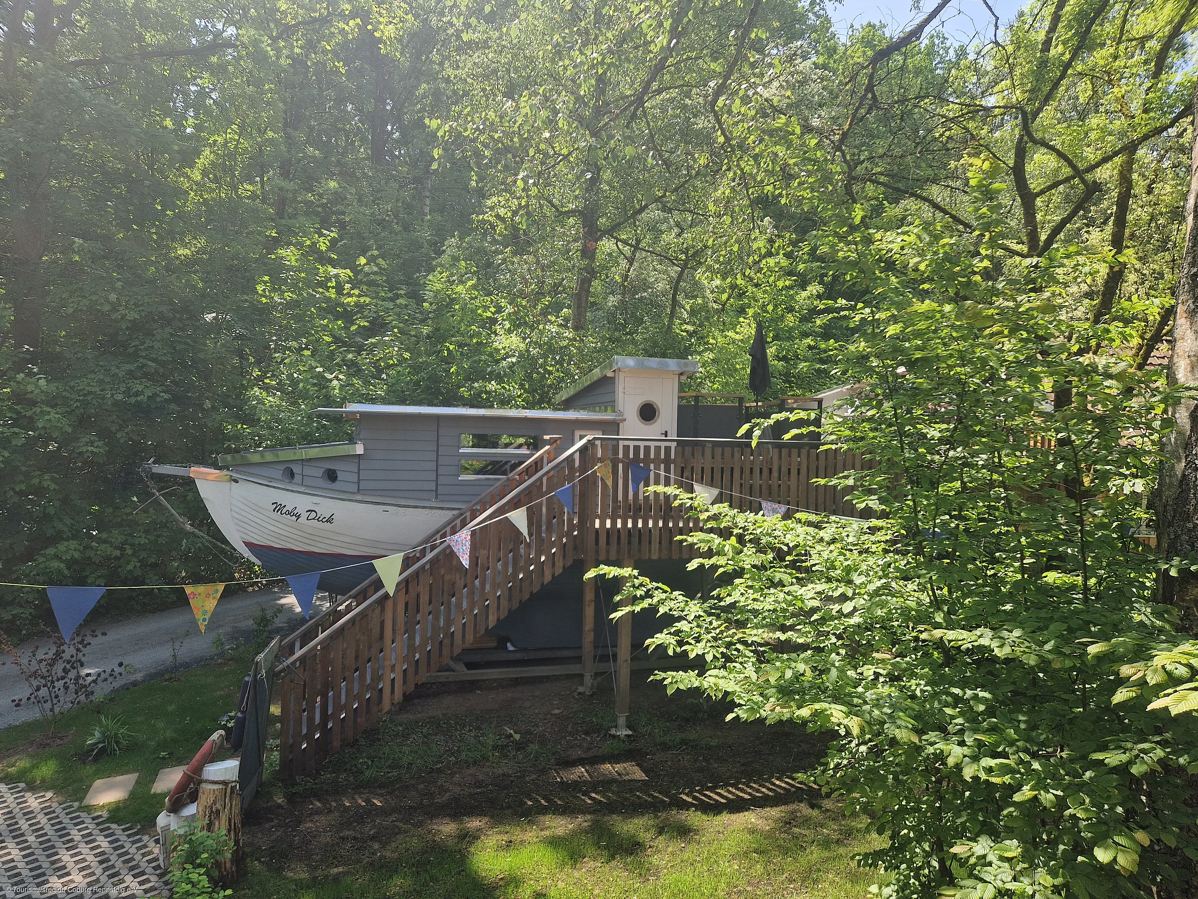 Haus in Form eines Bootes mit dem Namen Moby Dick, umgeben von Bäumen und einer Holztreppe mit Wimpelkette