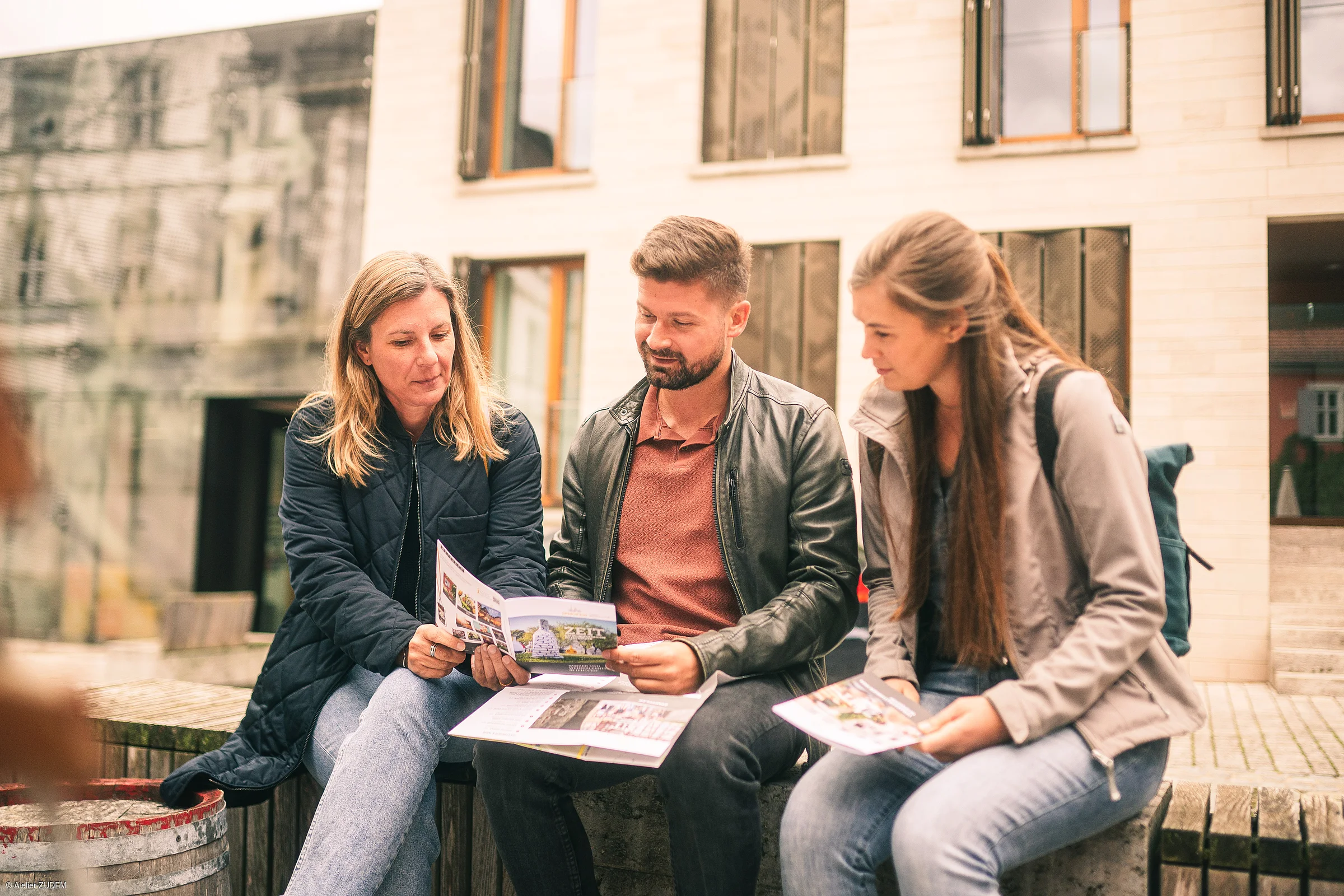 Drei Personen sitzen draußen auf einer Bank und schauen gemeinsam in Broschüren.