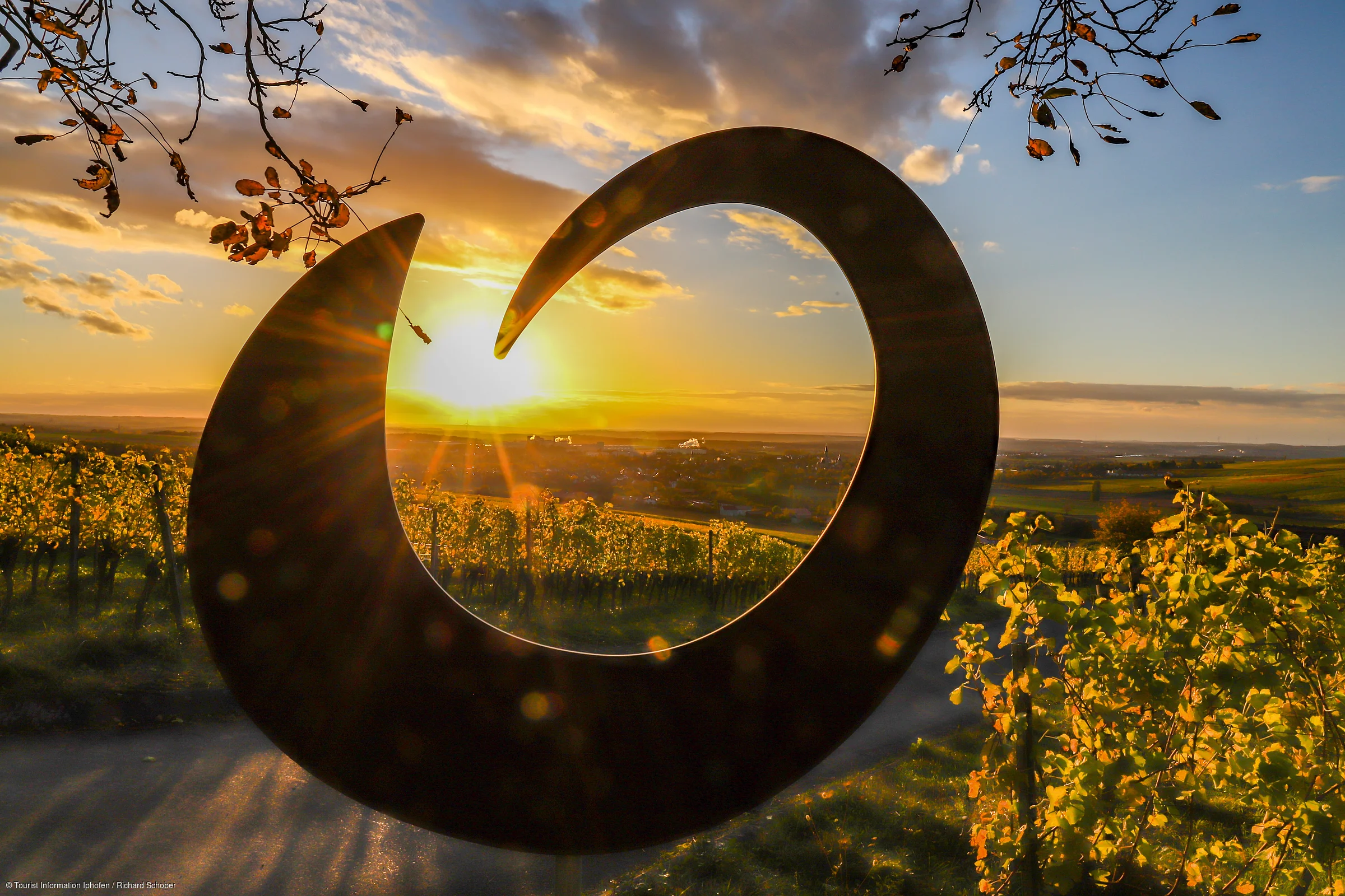 Schwarze Skulptur in Form einer Welle vor Sonnenuntergang über Weinbergen und Landschaft.