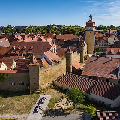 Blick auf eine Stadt mit historischen Stadtmauern, Türmen und roten Ziegeldächern bei klarem Himmel.