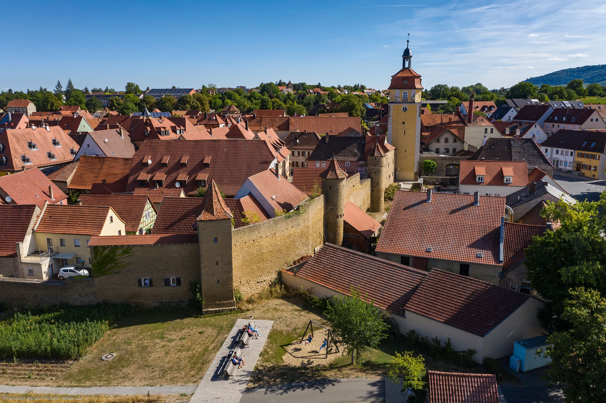 Blick auf eine Stadt mit historischen Stadtmauern, Türmen und roten Ziegeldächern bei klarem Himmel.