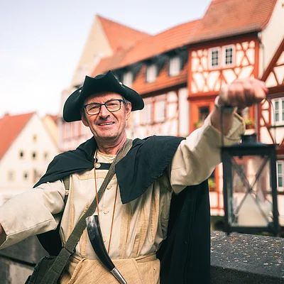 Mann in historischem Gewand mit Laterne und Hellebarde vor Fachwerkhäusern in einer Altstadt
