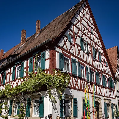 Fachwerkhaus mit grünen Fensterläden und zwei Personen auf Kopfsteinpflaster bei klarem Himmel.