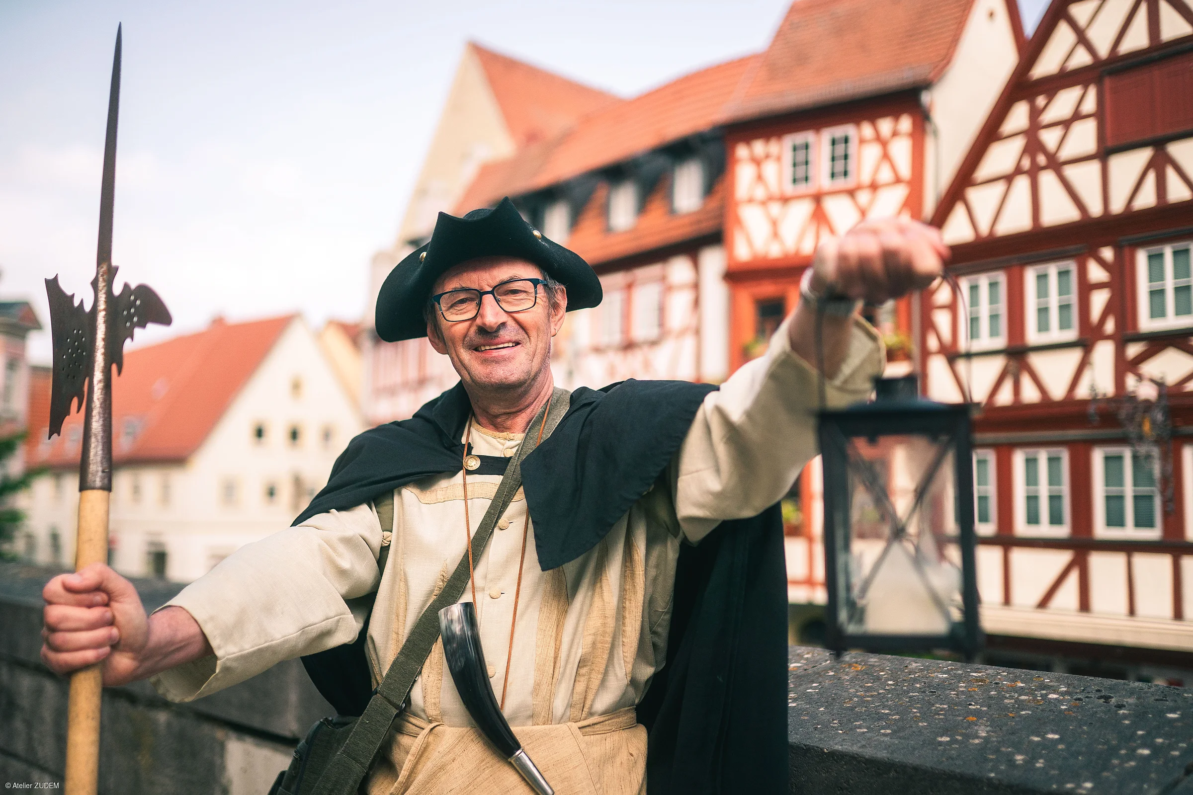 Mann in historischem Gewand mit Laterne und Hellebarde vor Fachwerkhäusern in einer Altstadt