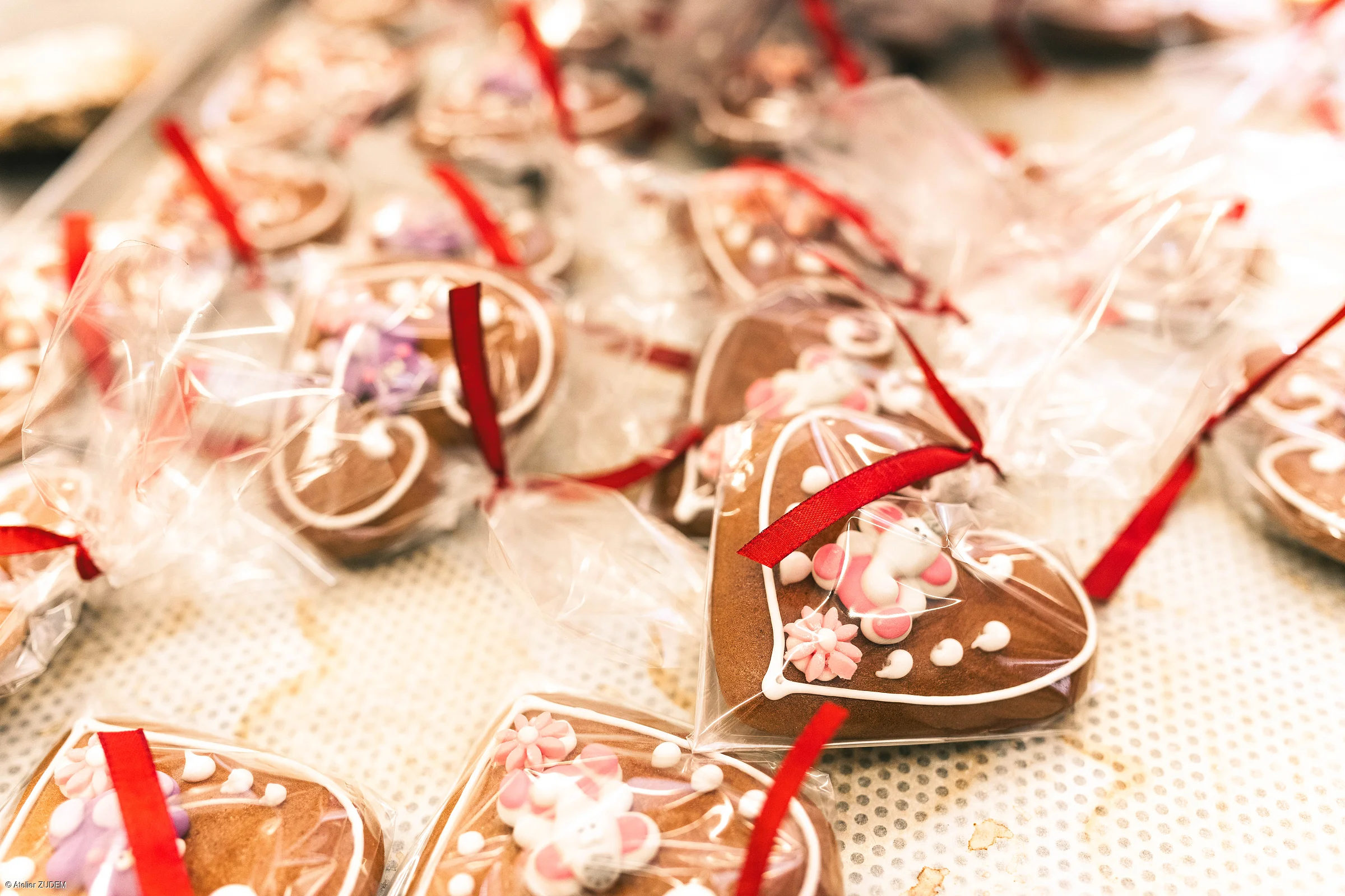 Mehrere verpackte Lebkuchenherzen mit Zuckerdekor und roten Bändern liegen auf einem Tisch.