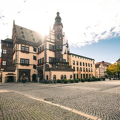 Historisches Rathaus mit Turm an einem großen gepflasterten Marktplatz bei Sonnenschein und blauem Himmel.