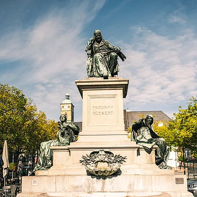 Denkmal von Friedrich Rückert mit drei Figuren auf einem steinernen Sockel im Freien bei Tageslicht