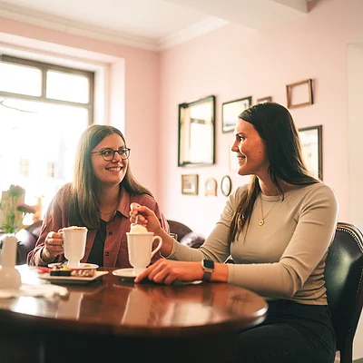 Zwei Frauen sitzen an einem Holztisch in einem Café und trinken heiße Getränke.