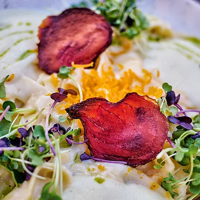 Teller mit Pasta, grünen Sprossen, geriebenem Käse und roten Gemüsechips, garniert mit grüner Sauce