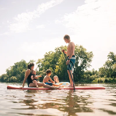Familie mit drei Kindern auf einem Stand-up-Paddle-Board auf ruhigem Gewässer bei Tageslicht