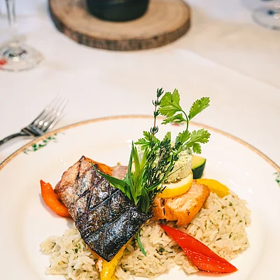 Gegrilltes Fischfilet auf Reis mit Paprika und Kräutern auf weißem Teller mit floralem Rand