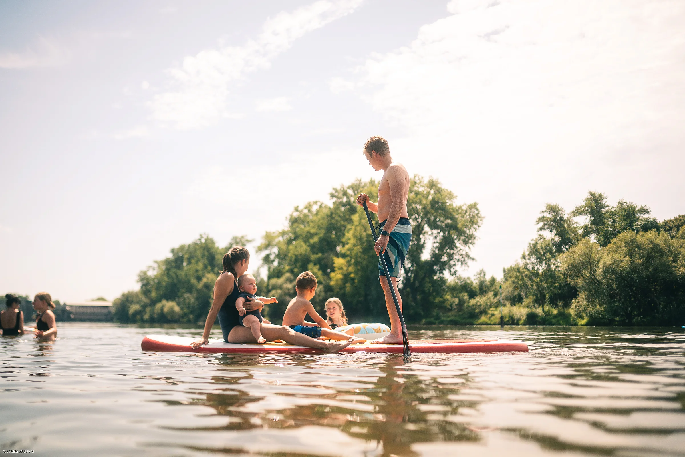Familie mit drei Kindern auf einem Stand-up-Paddle-Board auf ruhigem Gewässer bei Tageslicht
