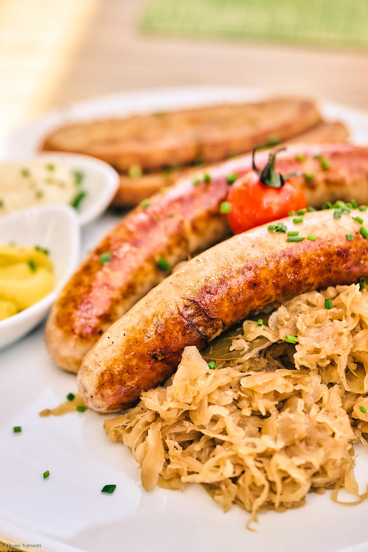 Zwei gebratene Bratwürste mit Sauerkraut, Senf, Soße und Brot auf weißem Teller.