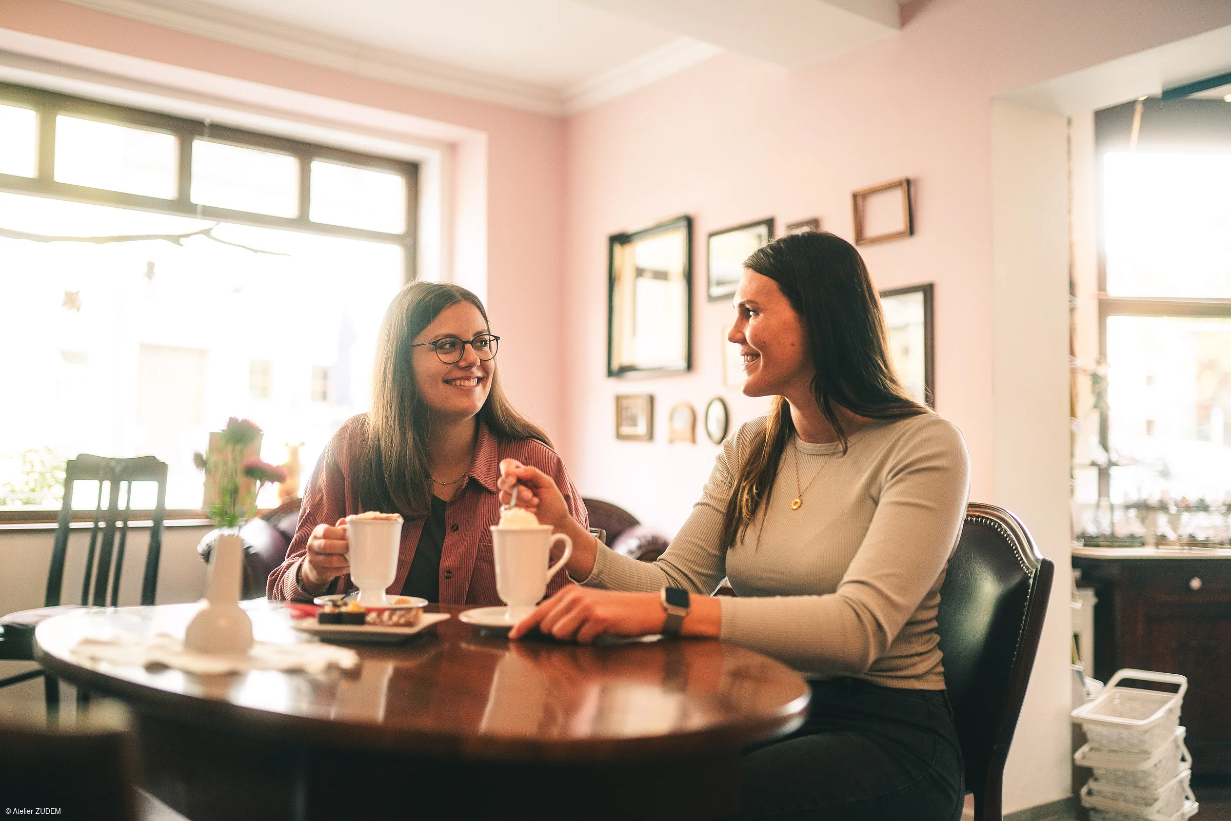 Zwei Frauen sitzen an einem Holztisch in einem Café und trinken heiße Getränke.